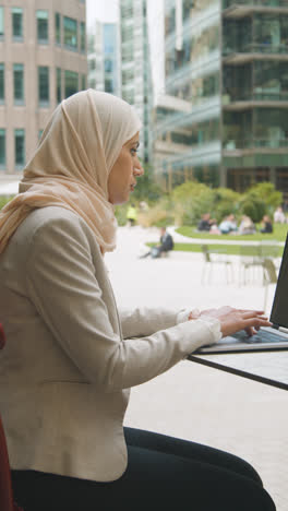 Vertikales-Video-Einer-Muslimischen-Geschäftsfrau,-Die-Draußen-In-Stadtgärten-Sitzt-Und-An-Laptop-2-Arbeitet